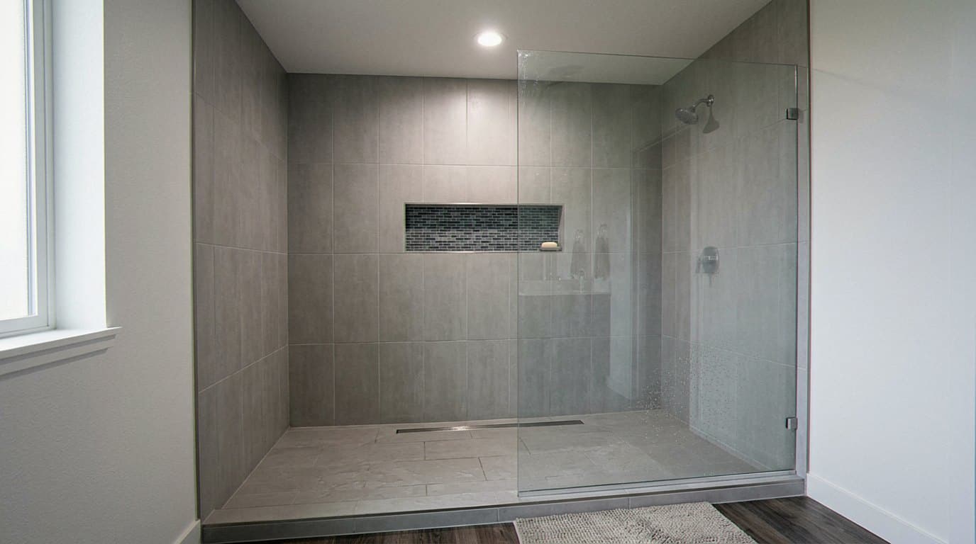 Gray tile walk-in shower with glass door and niche